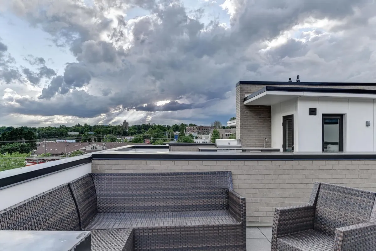The photo features an expansive rooftop seating area overlooking the city. The vantage point offers a broad perspective of the urban landscape, with clouds rolling overhead. The setting invites quiet relaxation, conversation, and taking in the dynamic city below.
