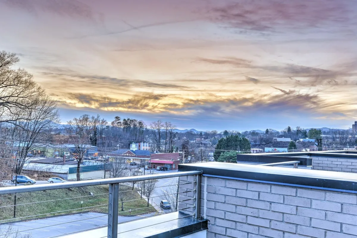 This view image spotlights a balcony overlooking Asheville’s cityscape at sunset, with distant mountains and a glowing sky. The perspective invites viewers to imagine relaxing outdoors while soaking in the vibrant urban energy and scenic beauty, reinforcing the idea of an adventure-filled yet tranquil home base.