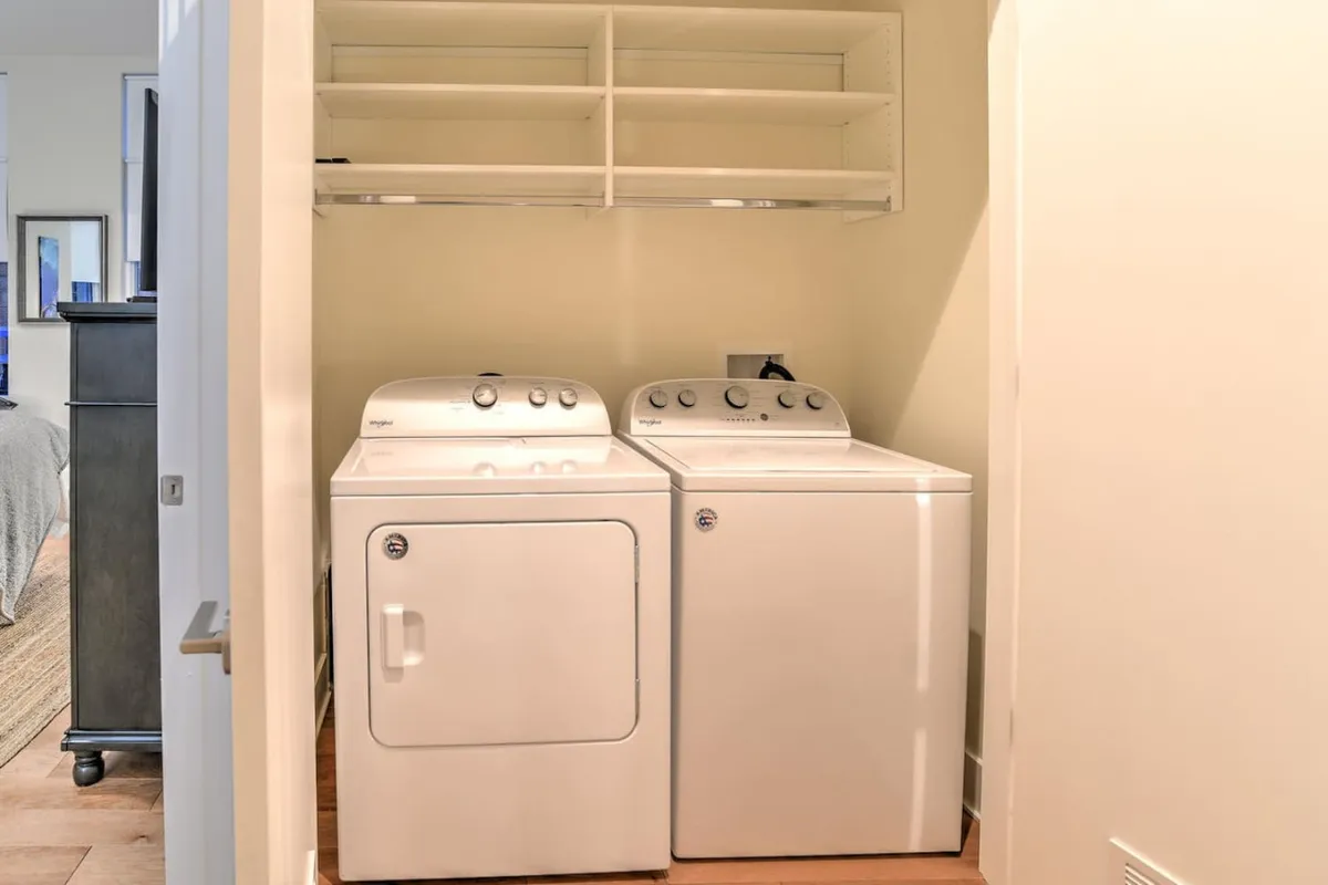 A dedicated laundry space featuring a modern washer and dryer, with open shelving for organization. The setup suggests practical convenience and is easily accessible for guests of all ages.