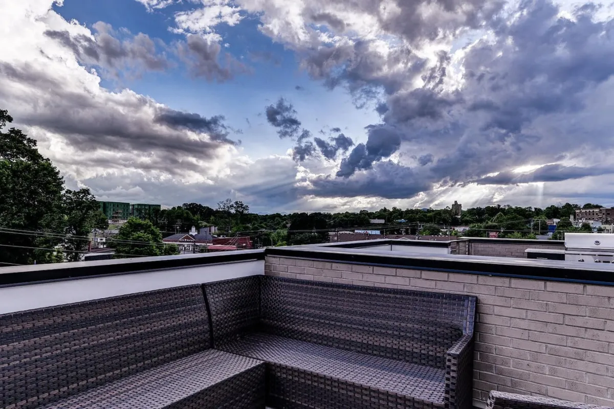 This image captures a serene rooftop seating area, with comfortable outdoor furniture set against a dramatic evening sky. The distant skyline and vibrant sunset colors create a striking urban panorama, and the elevated vantage point highlights the exclusivity and tranquility of the terrace.